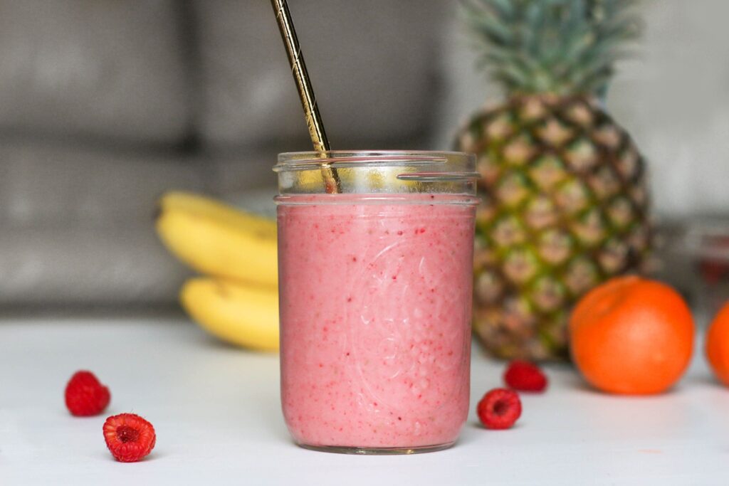Queen Garnet Mango Smoothie in a glass on a table, surrounded by fresh fruit