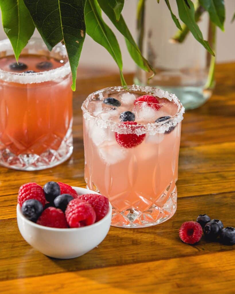 Plum + Berry 0% Sangria in a glass with bowl of raspberries alongside