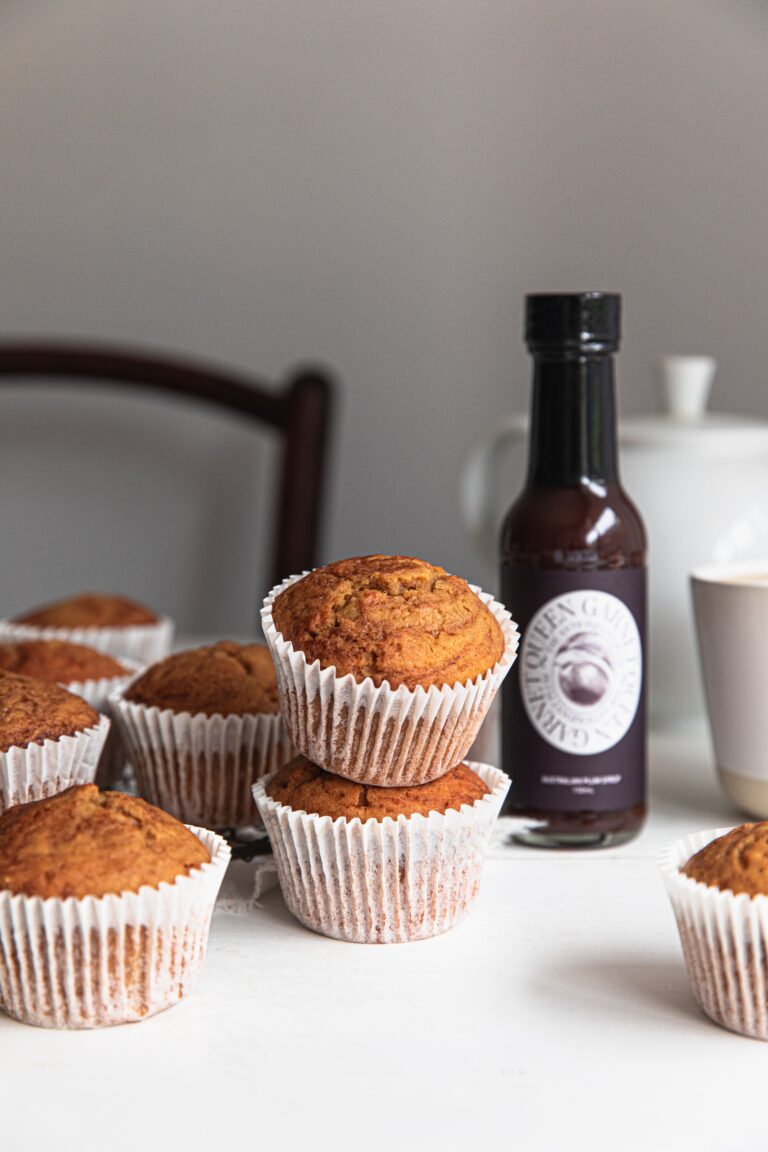 Stacked plum swirl muffins beside bottle of Queen Garnet Syrup