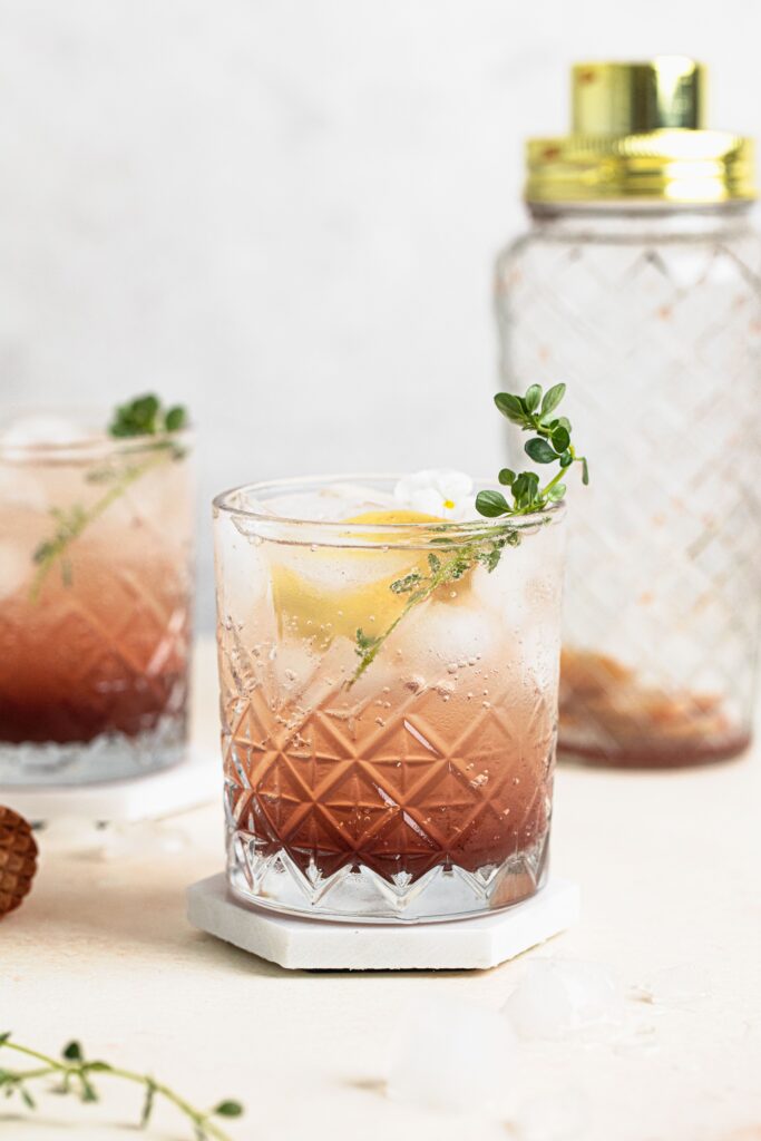 Spiced plum lemonade in glass with sprig of lemon thyme