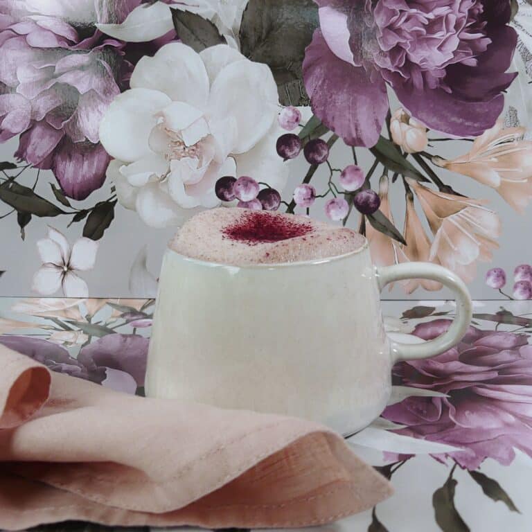 A mug of Queen Garnet Plum latte against a floral backdrop.